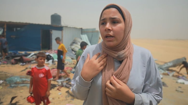 A woman in a blue shirt with a pink headscarf stands in what was once a tent camp in Gaza.