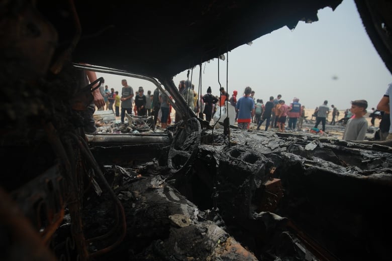 The charred interior of a burned car is visible.