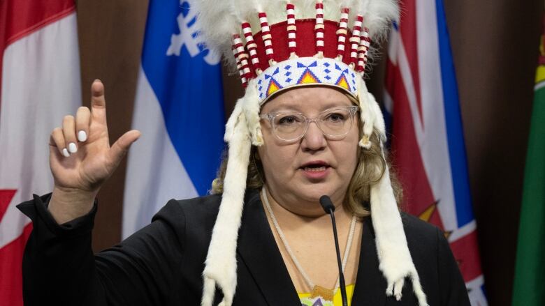 A woman with glasses wearing an Indigenous headdress at a podium.