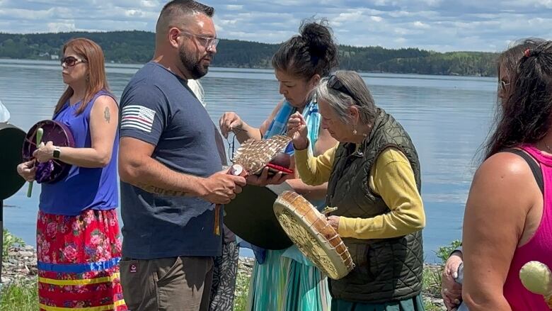 A man wearing a blue shirt and holding a feather stops in front of a woman wearing yellow holding a hand drum for a smudge.