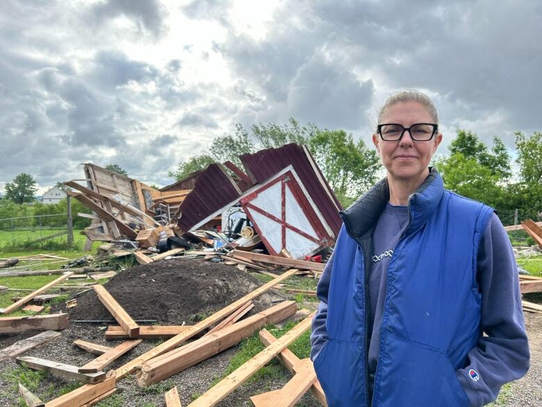 A woman stands on her property in front of a collapse barn. 