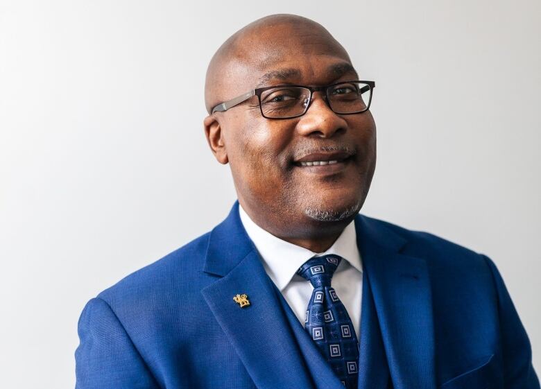 A Black man smiling for a portrait wearing a blue suit. 