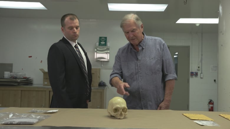 Two men look at a human skull on a table