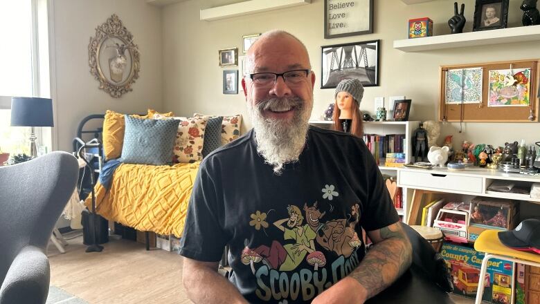 A man in a wheelchair smiles at the camera in his room