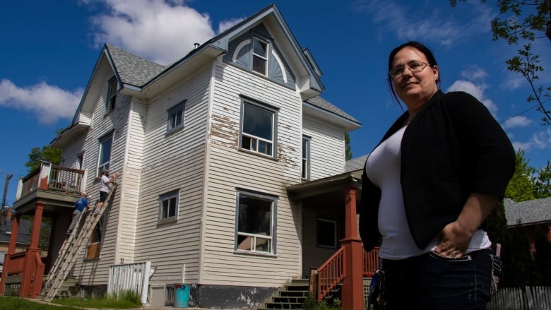 A woman stands in front of a house being renovated.