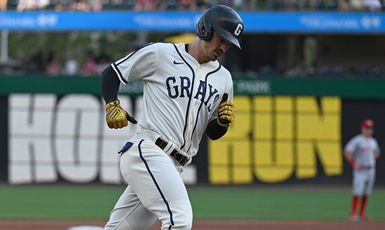 A baseball player wearing a helmet and uniform is shown rounding third base.