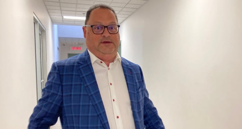 Man in blue plaid suit jacket in a hallway, looking at the camera.