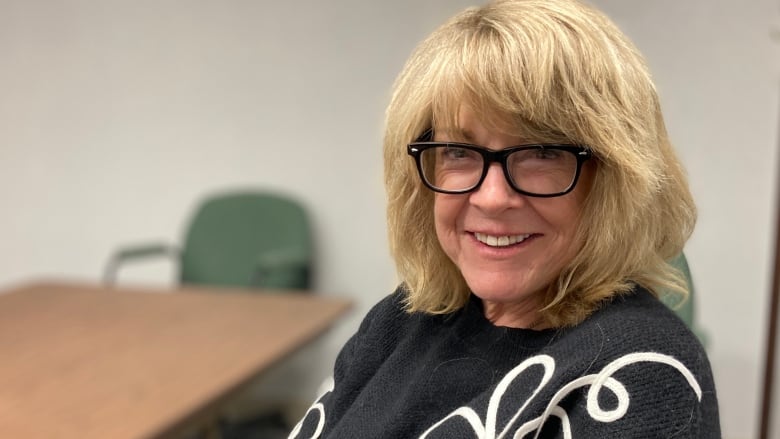 Woman with shoulder-length blond hair and black-rimmed glasses smiles at the camera.