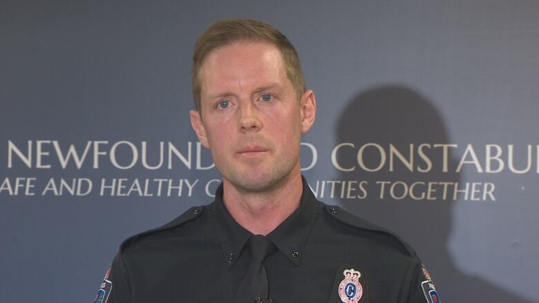 A police officer stands in front of a navy blue wall.