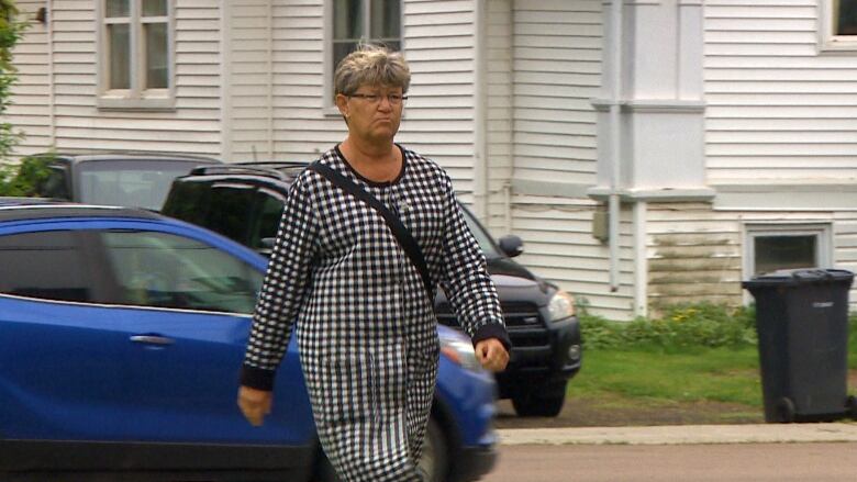 A woman walks past the camera with a black and white dress on. She has short hair and a blank face. 