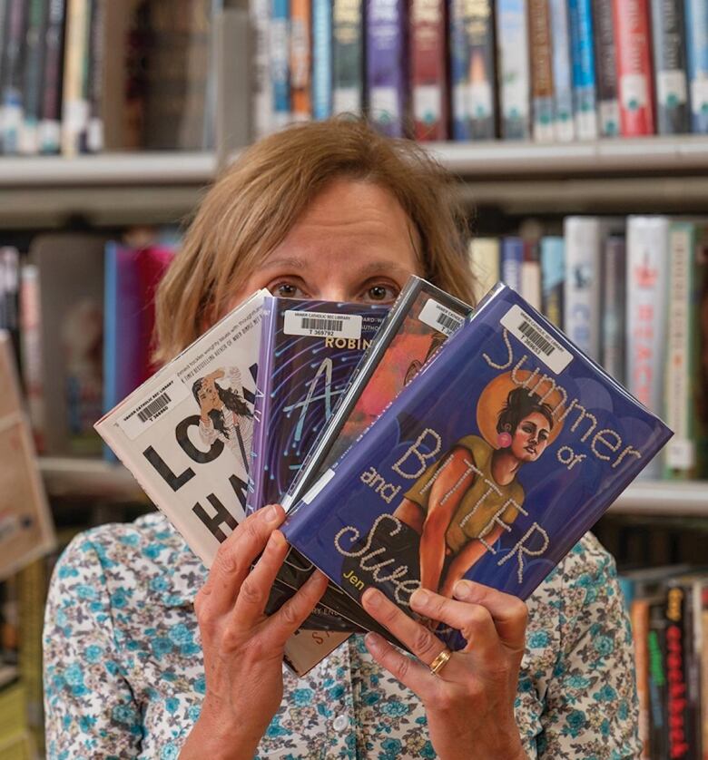 Person peering at camera behind a stack of four books they are holding up.