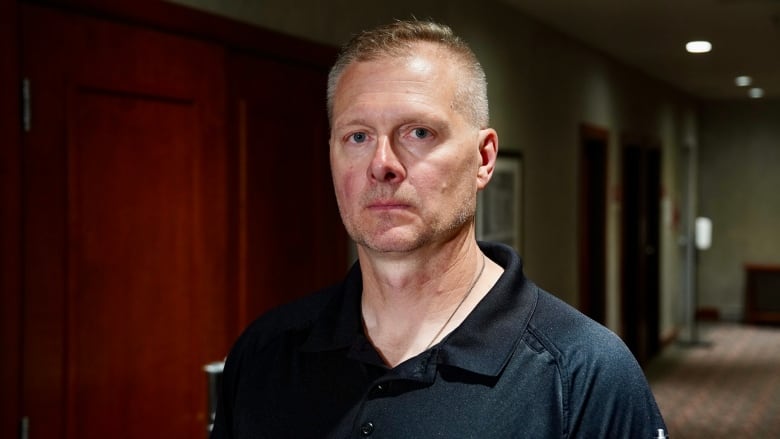 A man wearing a black t-shirt looks at the camera.