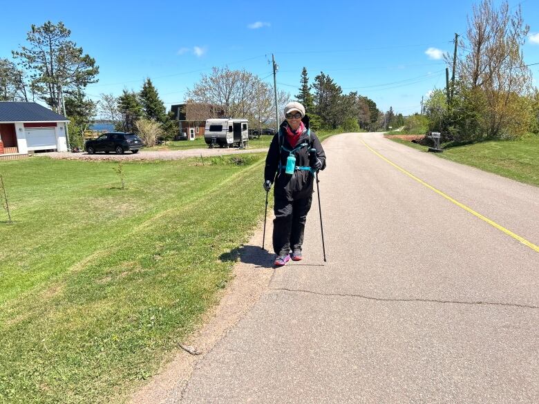 A woman in long-distance walking gear walks down a road on a sunny day