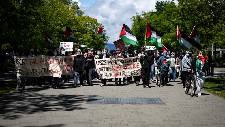 A group of people waving red, white, black and green Palestinian flags and holding a sign that says 