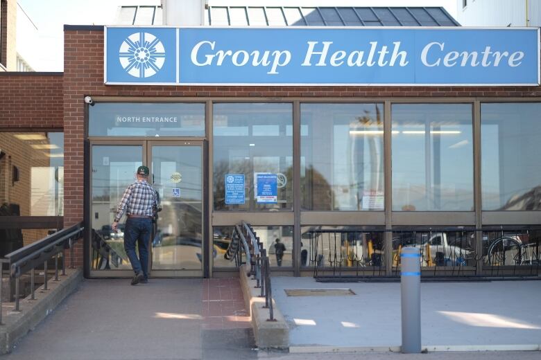 A man in a plaid shirt walks in to an office building with a sign reading Group Health Centre