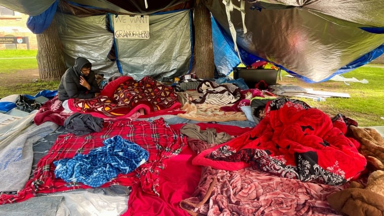 Protest camp showing one person awake and other sleeping under colourful blankets.