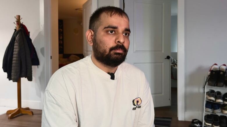 A man sitting in his apartment wearing a white long sleeve shirt