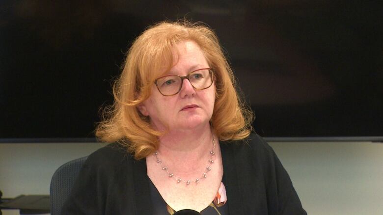 A woman with red hair wearing a black shirt sitting inside a board room. 