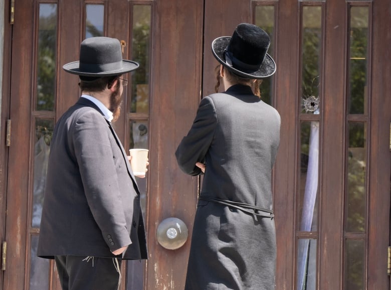 Two men have their backs to the camera. They look at a hole in a door.