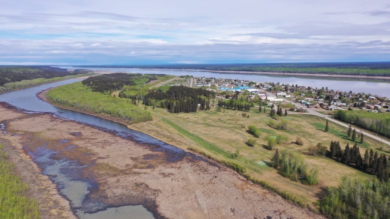 A small community is seen from afar, beside a wide river.