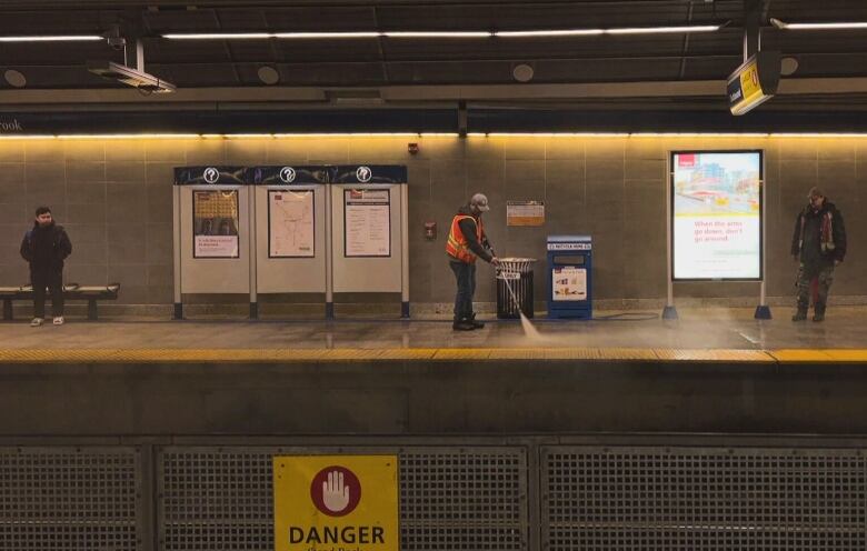 A man in a vest uses a power washer on the train platform. 