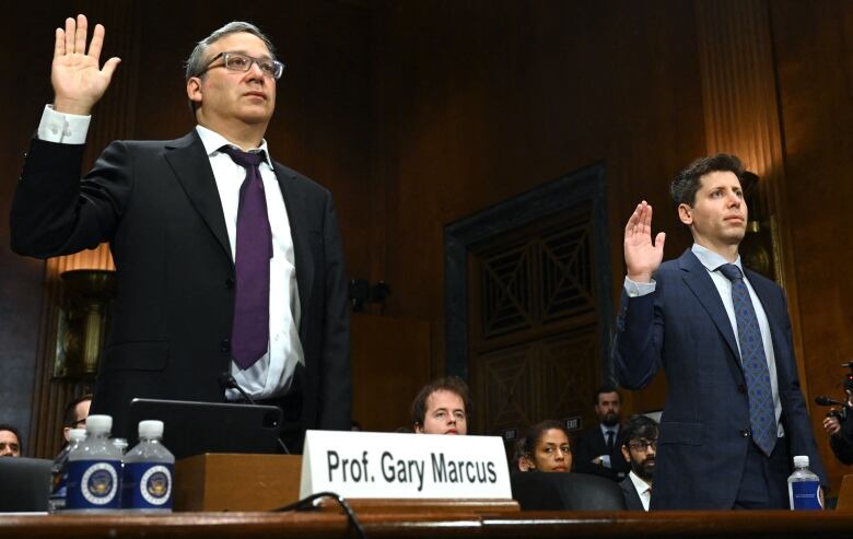 Two men wearing suits raise their right hands as they are sworn in.