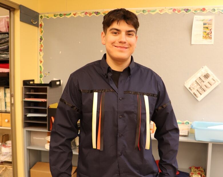 A young man stands wearing a ribbon shirt.