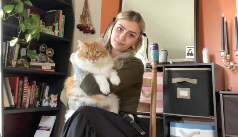 A person with long hair sitting in a chair holding a fluffy orange and white cat.