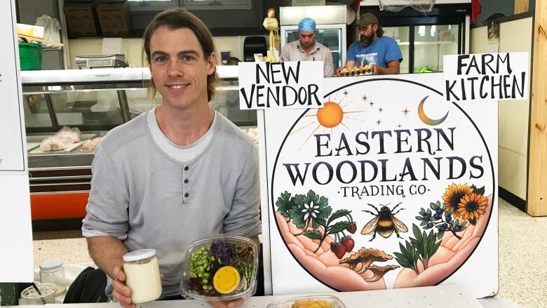 A farmer's market vendor sits in front of a table filled with power bowls and salads.