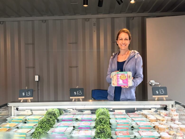 A woman stands in front of a table of grab-n-go meals.