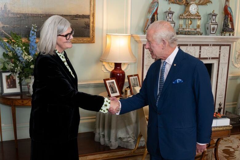 Two people shake hands in a living room.