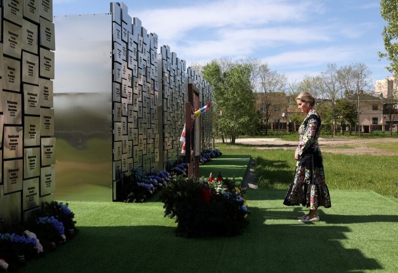 A person stands with their head bowed in front of a memorial wall.