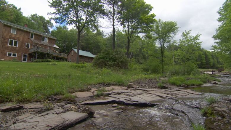 The back of a brown, 2-storey house overlooking a running creek.