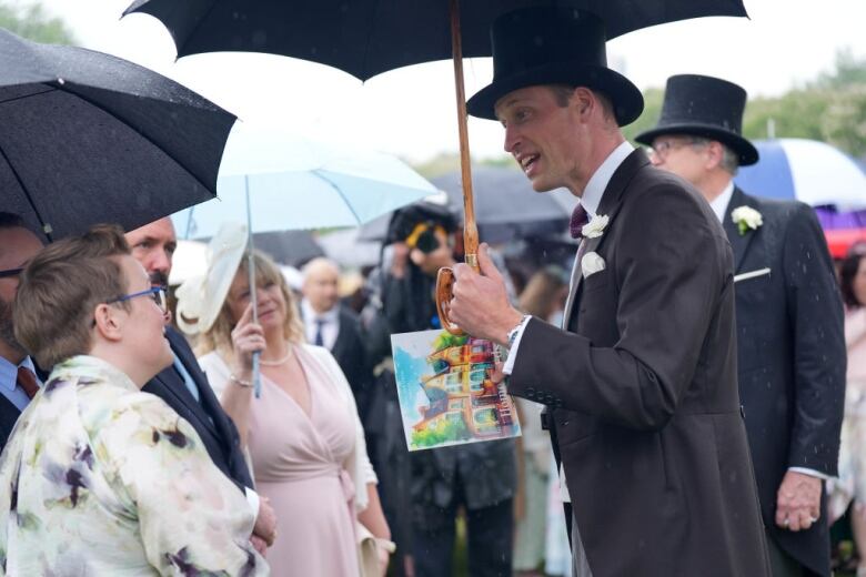 A person holding an umbrella and a drawing talks to others holding umbrellas as they stand on a lawn behind a large stone building.