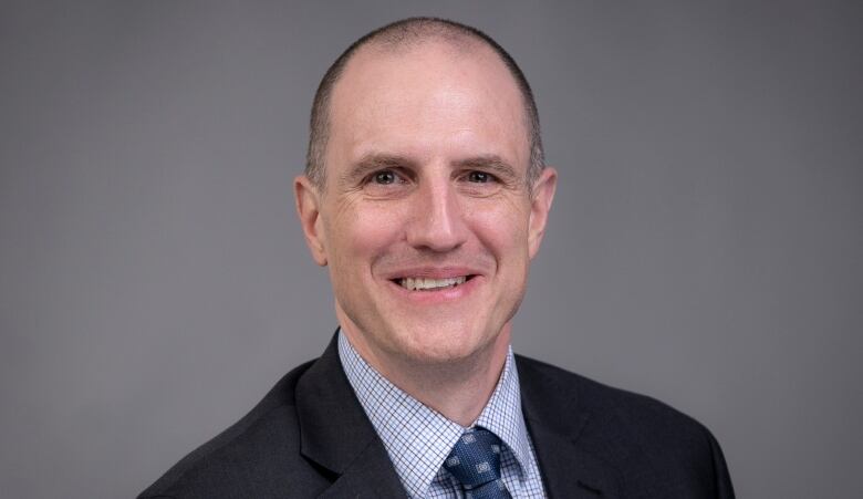 Dr. Keith Lehman is smiling, wearing a black suit and tie, as he looks directly into the camera.