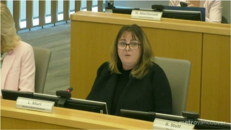 A woman in black clothing speaks at a board meeting.