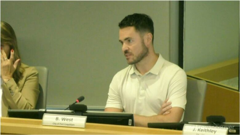 A man in a short-sleeved shirt speaks into a microphone at a board meeting.