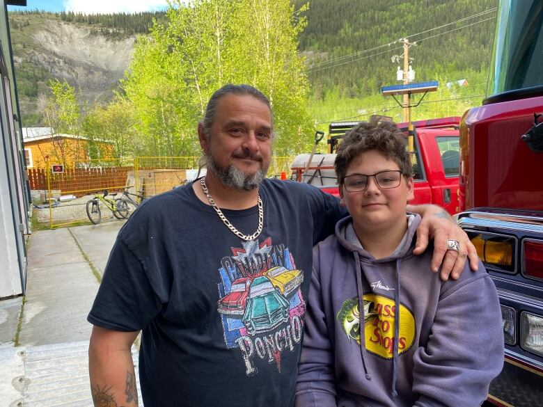 A man, and boy standing together infront of a fire truck.