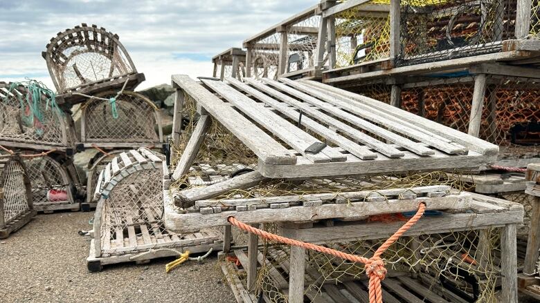 Several wooden lobster traps stacked on a wharf, some with the wood frame smashed, others with the mesh cut open.