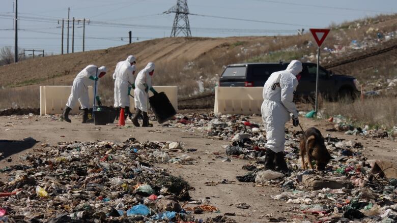 People in white hazmat suits sort through garbage that has been spread out on the ground.