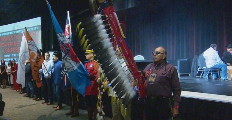 A lineup of people holding ceremonial staffs and flags.