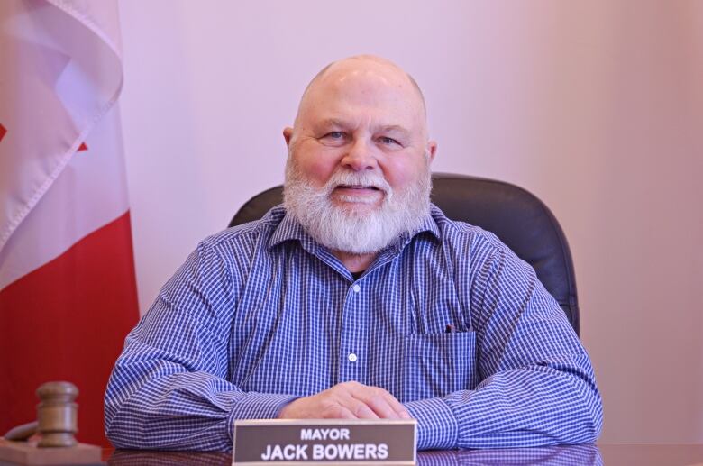 Man with white beard sits at a table with a name plate that says 'Mayor' in front of him.