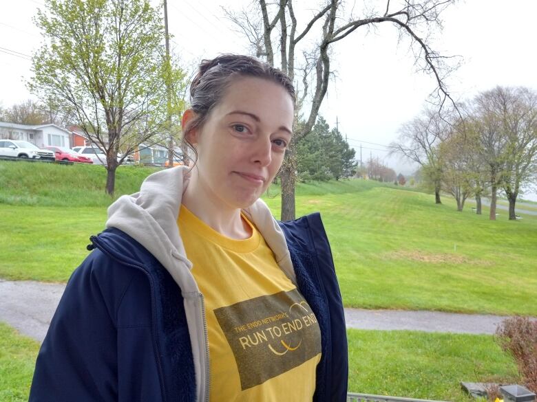 Woman with brown hair pulled back wearing a dark jacket with a yellow shirt that says 