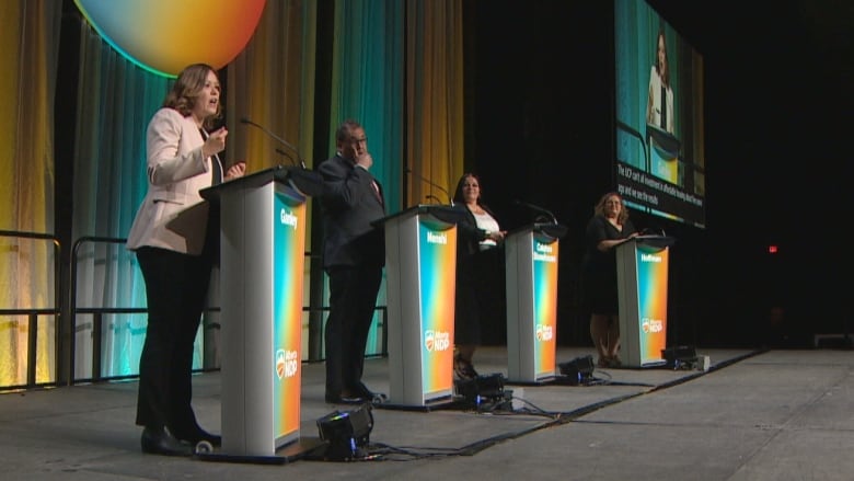 Four people stand on a stage behind lecturns. 