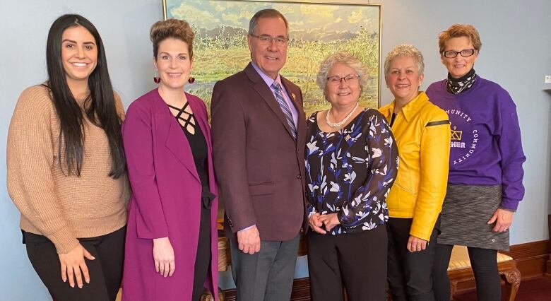 Six people stand in front of a lush green painting.