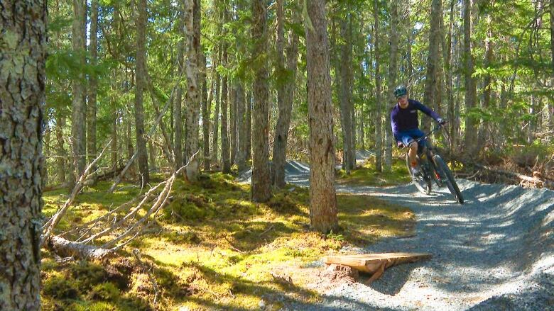 A teenager on a mountain bike, wearing a blue shirt, rides his bike in a forest trail.