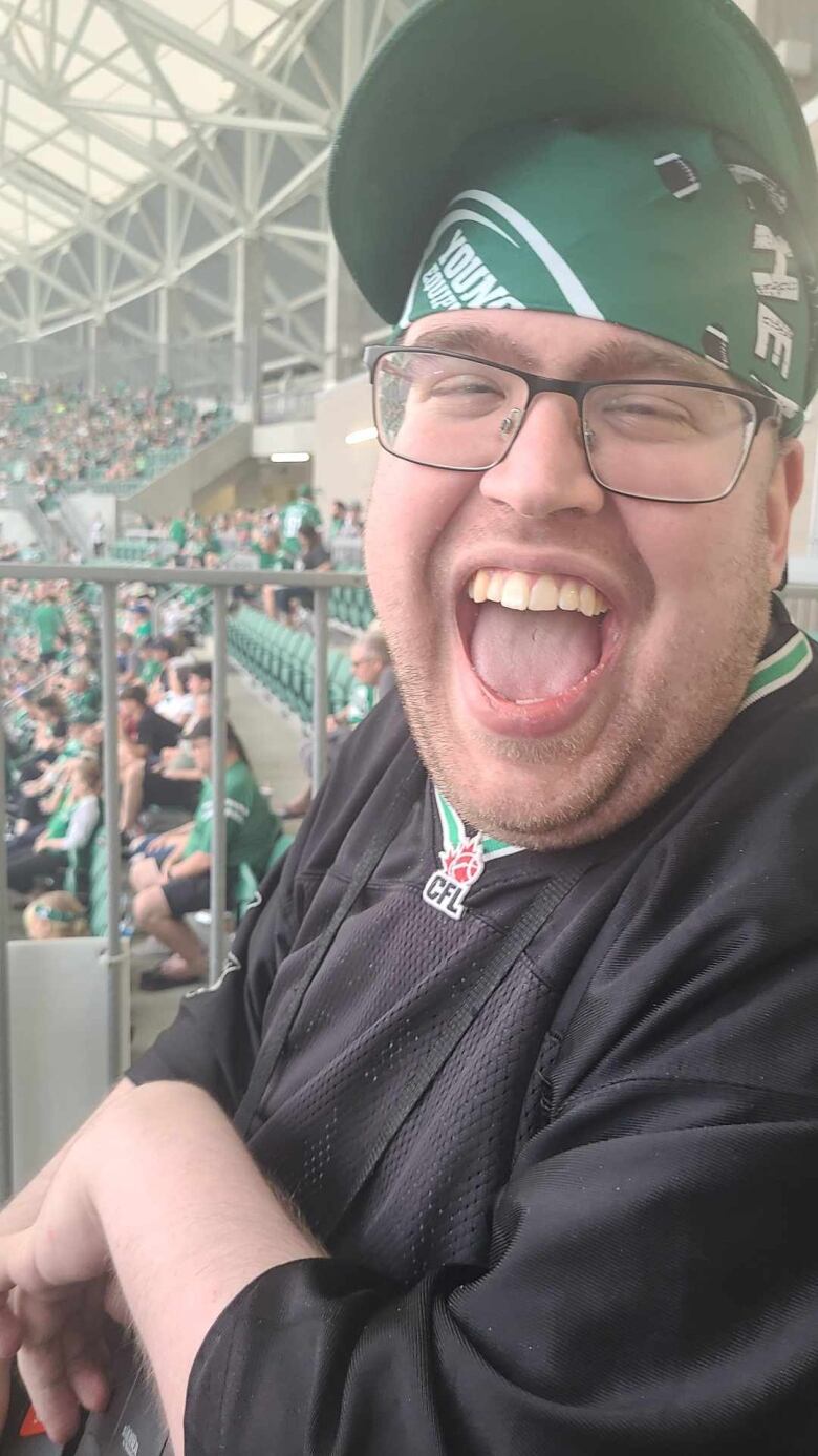 A closeup of a fan in glasses and a green hat cheering.