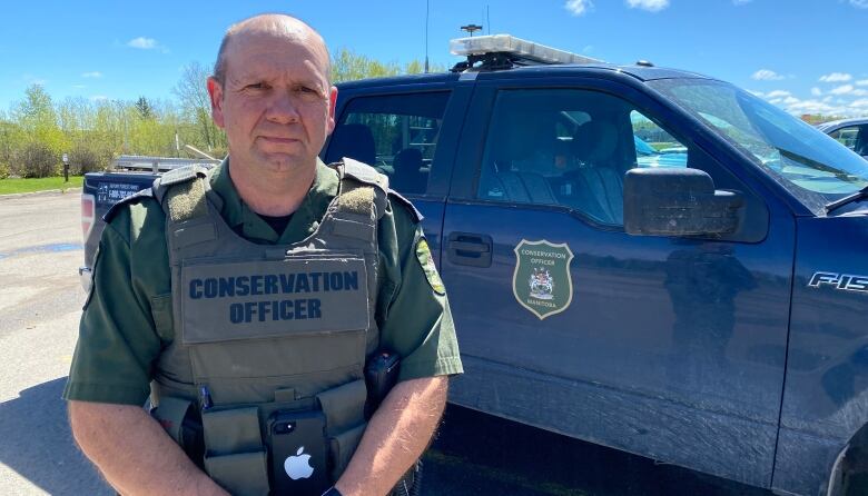 A man stands in a uniform outside a truck. Sunny day.