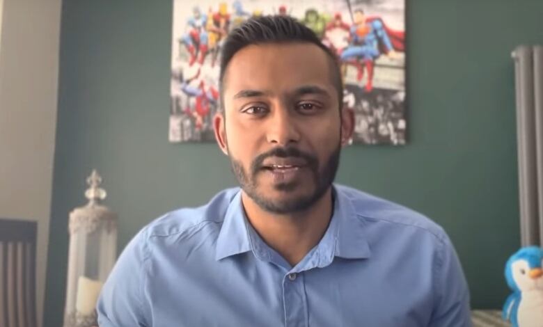 A man in a blue collared shirt is seen looking forward.