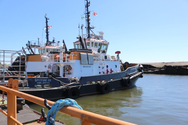 A tugboat moored along a pier with a yellow railing and blue rope. 